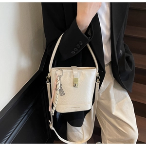 Détail d'un sac seau blanc crème avec un fermoir en métal doré et un ornement tressé