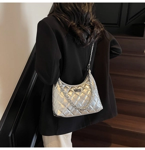 Detail of silver metallic quilted shoulder bag with chain strap and twist lock on model