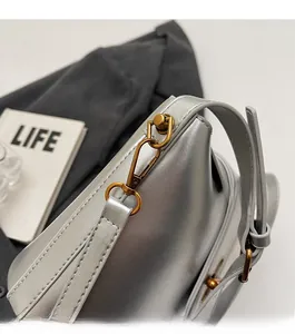 Detail of golden metal hooks and shiny silver fabric on a minimalist shoulder bag