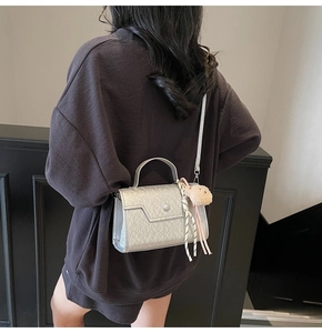 Silver textured crossbody bag with pink plush bear charm worn by a model