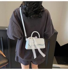 Detail of light blue crossbody bag with white lace ribbon and pearl charm on a model