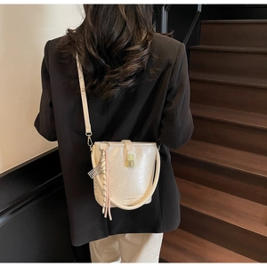 Détail d'un sac seau blanc cassé avec fermoir doré et bandoulière tissée sur un mannequin