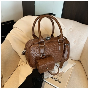 Detail of a brown woven leather bowling bag with silver zipper and mini charm accessory