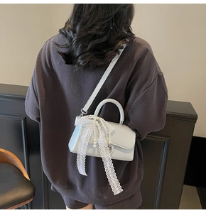 Close-up of light blue crossbody bag featuring white lace bow and pearl tassel detail