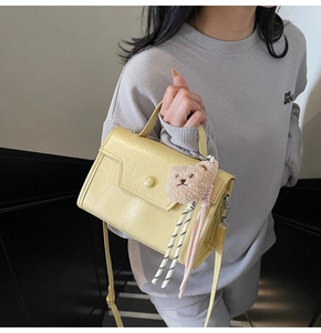 Detail of light yellow retro square bag with asymmetric flap and plush bear charm