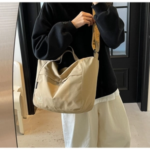 Detail of a beige canvas tote bag with a small dog logo and adjustable wide strap