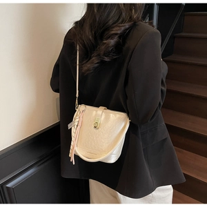 Détail du sac seau en cuir beige avec fermoir doré et foulard porté par un mannequin