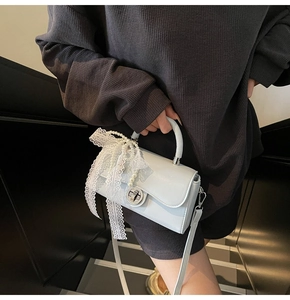 Close-up of a light blue crossbody bag with delicate lace and pearl bow charms on a model