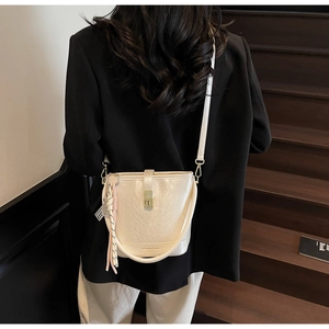 Sac seau beige avec fermoir doré et pendentif à pampilles porté par le modèle