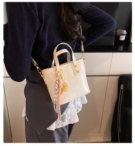 Detail of cream bucket bag with tennis racket charm and gold hardware on shoulder