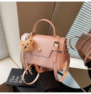 Detail of light pink crossbody bag with a cute plush bear pendant and textured finish