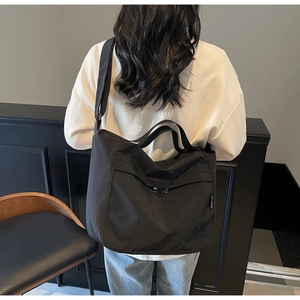 Detail of black nylon tote bag featuring adjustable strap and side brand label