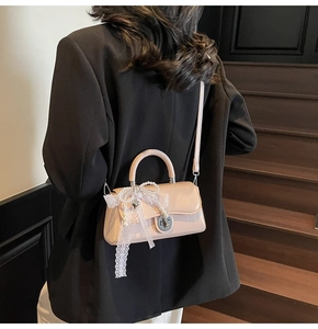 Detail of light beige crossbody bag with silver twist lock and lace butterfly pendant