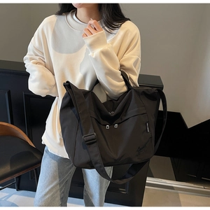 Detail of black nylon tote bag showing adjustable shoulder strap and zip pocket