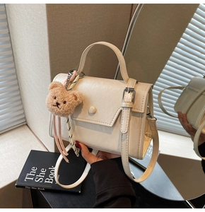 Detail of cream square handbag with leather texture and cute brown bear pendant