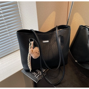 Dettaglio della trama intrecciata di una borsa nera con ciondolo a orso e logo in metallo