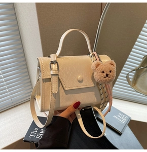 Detail of cream square crossbody bag with plush bear charm and striped silk scarf wrap