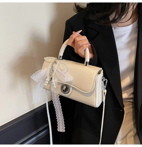 Detail of creamy white crossbody bag with elegant lace bow and pearl charms