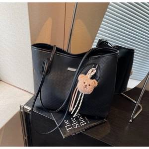 Dettaglio della borsa shopper nera intrecciata con logo metallico e ciondolo a orsetto