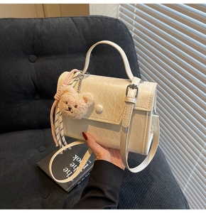 Detail of cream square crossbody bag with lychee texture and cute bear charm
