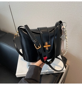 Detail of black crossbody bucket bag with golden twist lock and woven knot charm
