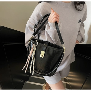 Détail d'un sac seau noir avec fermoir doré et un pendentif en corde tressée colorée