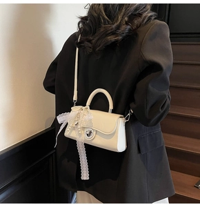 Creamy white crossbody bag with lace bow and pearl pendant shown on a black suit