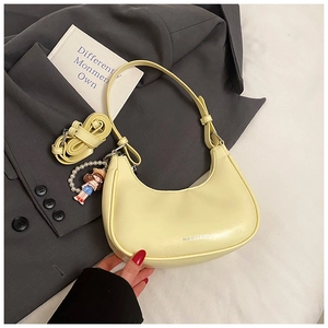 Detail of pale yellow crescent hobo bag with pearl charm on grey blazer backdrop