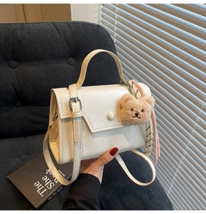 Detail of cream leather handbag with pink striped silk scarf and plush bear charm