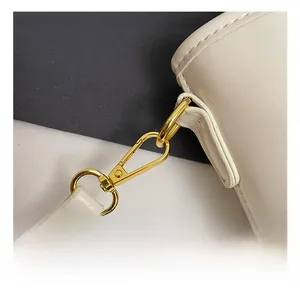 Close-up of golden metal strap hook and fine stitching on a cream bucket bag