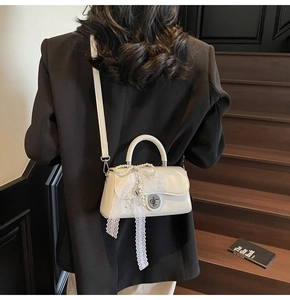 Detail of cream white small square bag with pearl chain bow and heart pendant on a model