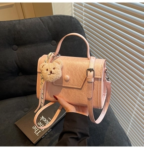 Pink crossbody bag with cute plush bear and striped scarf on a black velvet sofa