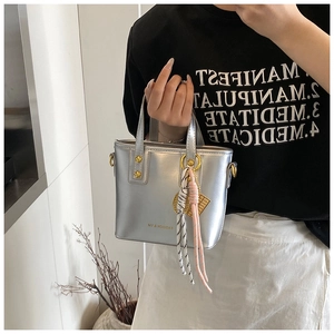 Close-up of metallic silver tote bag featuring woven charms and gold hardware detail