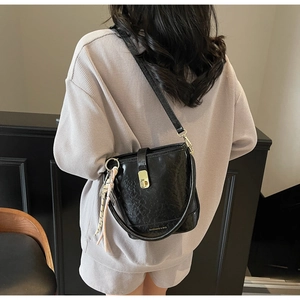 Détail du sac seau noir avec fermoir doré et pendentif tressé porté par le modèle