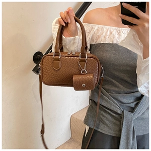 Detail of dark brown woven textured bowling bag with mini pendant and adjustable strap