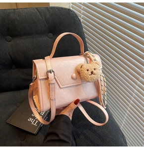 Detail of light pink square handbag with fuzzy bear charm and silk scarf handle decor