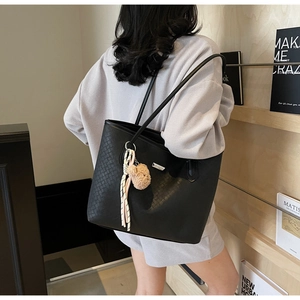 Dettaglio di una borsa tote in pelle intrecciata nera con ciondolo a orsetto e logo in metallo