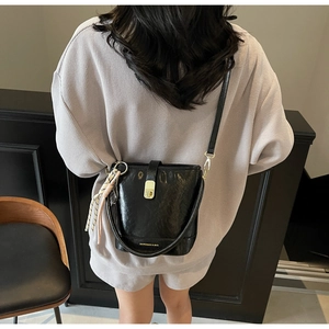 Détail d'un sac seau en cuir verni noir avec fermoir doré et cordon rayé sur le mannequin