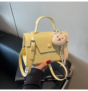 Detail of yellow crossbody bag featuring matte texture and a cute plush bear charm