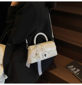 Close-up of cream square handbag with white lace bow and elegant pearl bead detailing
