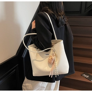 Dettaglio della borsa tote intrecciata bianco panna con ciondolo a orsetto e logo