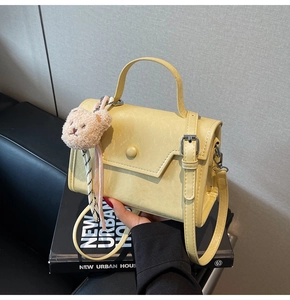 Detail view of cream small crossbody bag with a cute plush bear pendant and top handle