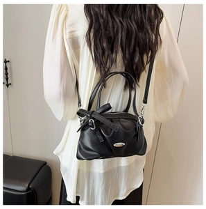 Détail du sac bandoulière en cuir noir avec nœud et plaque métallique argentée