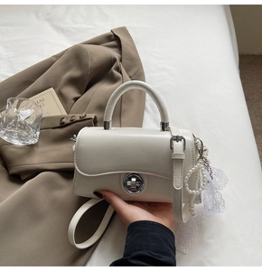 Detail of creamy white leather handbag with silver twist lock and pearl bow charm