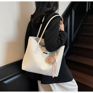 Dettaglio della borsa tote bianca intrecciata con logo in metallo e ciondolo orso