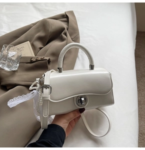 Detail of a creamy white handbag with a pearl lace pendant and metallic twist lock clasp