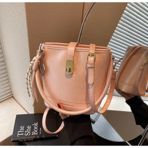Détail du sac seau rose en cuir grainé avec fermoir rotatif doré et pendentif décoratif