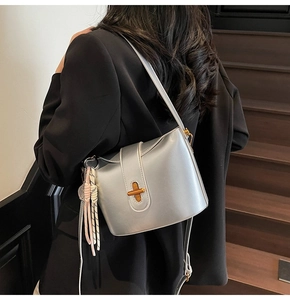 Detail shot of silver metallic bucket bag with golden cross clasp and braided rope charm