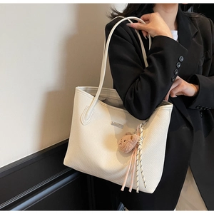 Dettaglio borsa tote bianca intrecciata con ciondolo a forma di orso e nastro a righe