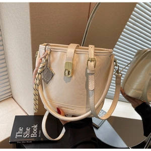 Détail du sac seau crème avec fermoir doré et pendentif tissé sous lumière douce